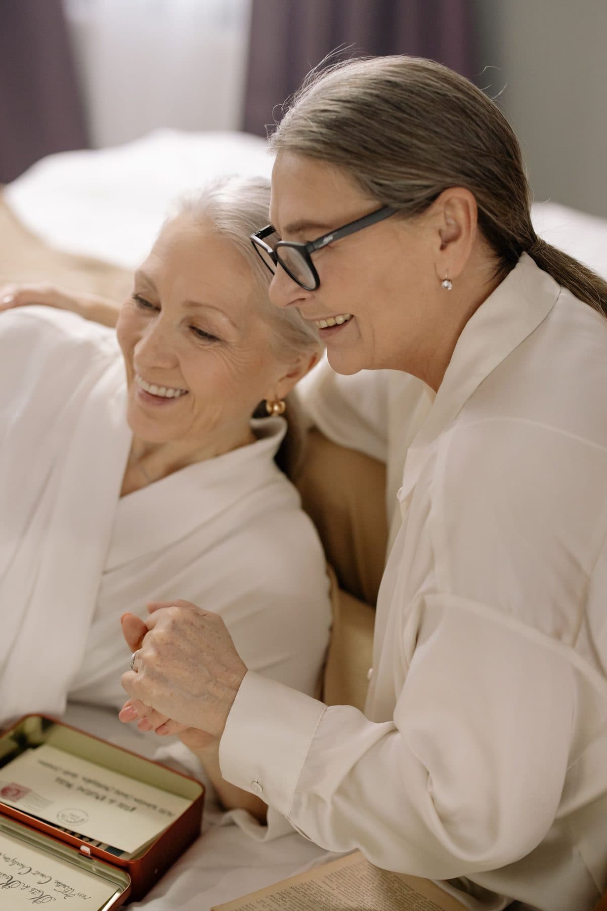 Dos mujeres, una al lado de la otra, sonriendo sobre una caja de recuerdos y cartas.